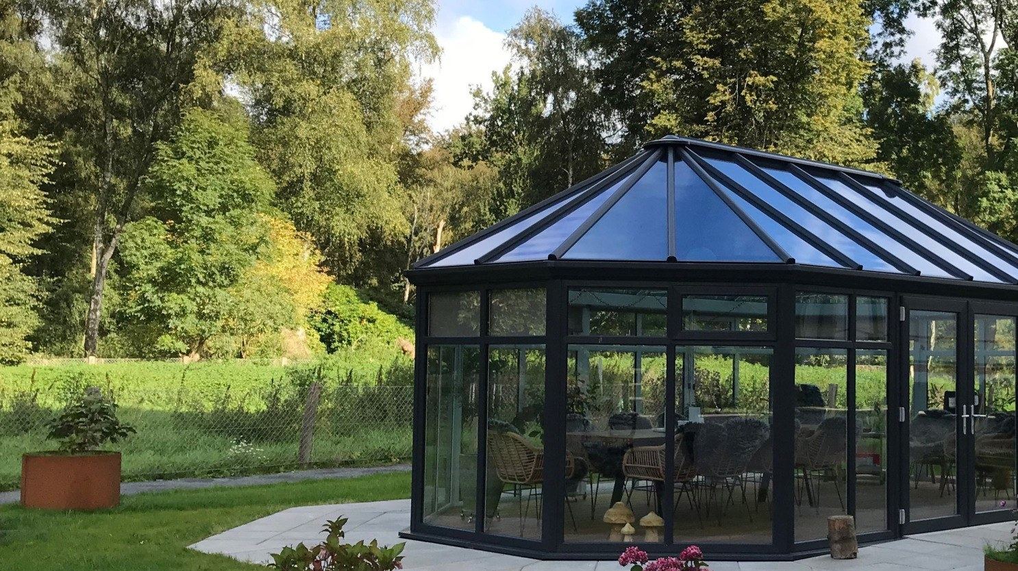 An octagonal dark-framed garden building surrounded by trees